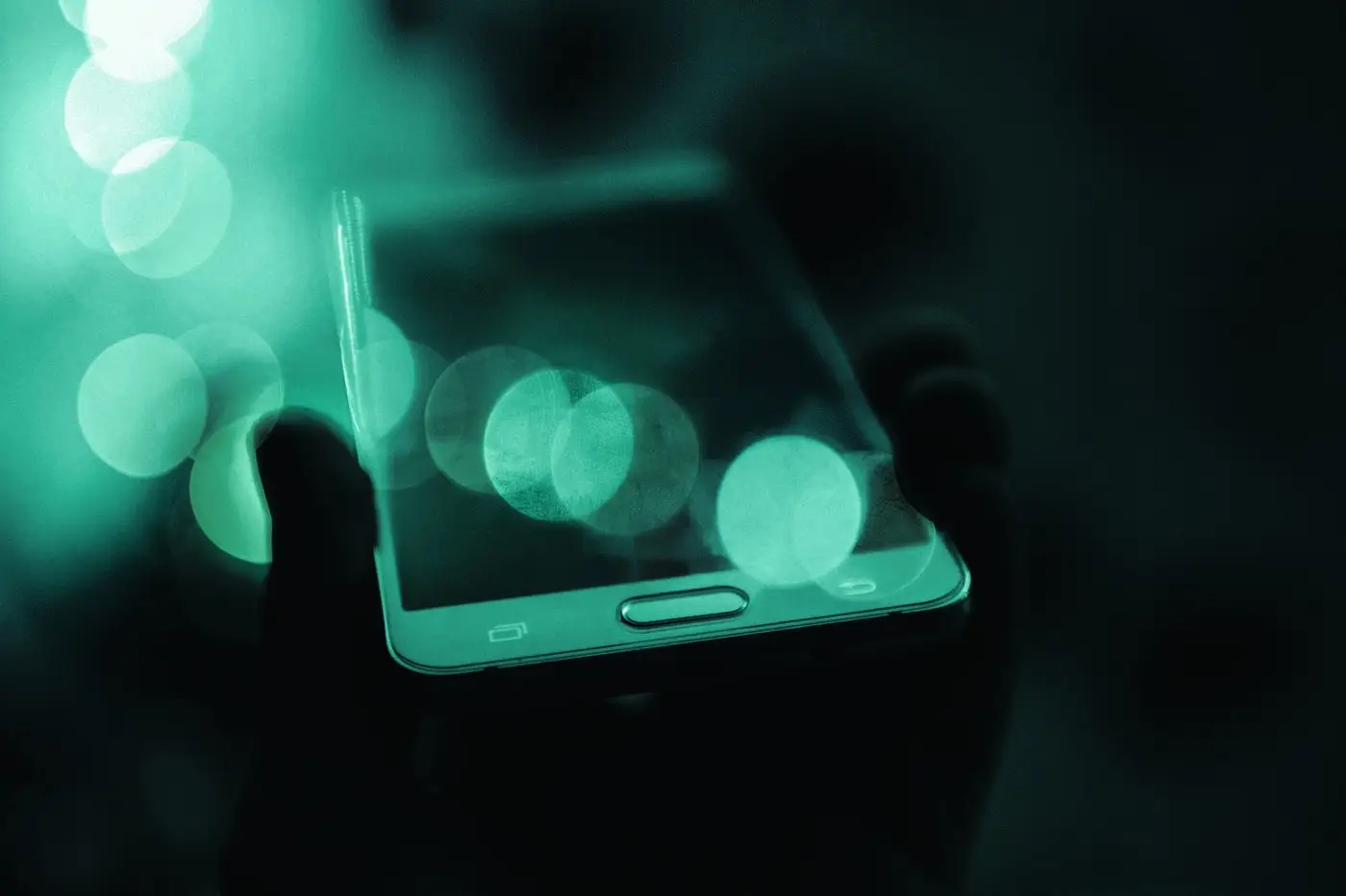 Hand holding a smartphone surrounded by glowing bokeh lights